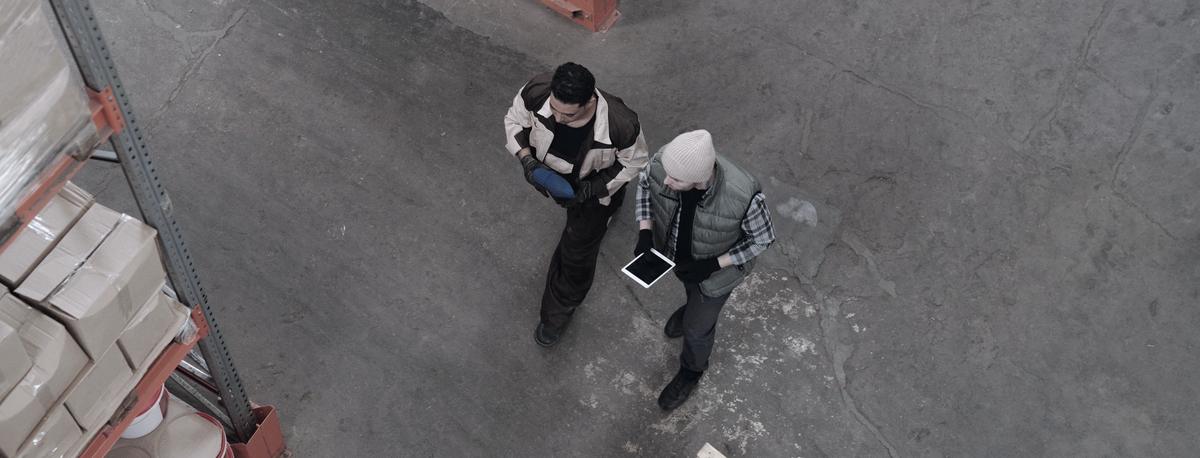 Dvaja ľudia prechádzajú uličkou skladu a nad tabletom riešia zásoby